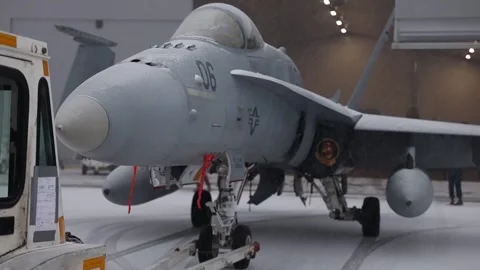 Tug reverse pushing U.S. Marines F/A-18 Hornet aircraft into hangar in the snow Stock Footage 256638538