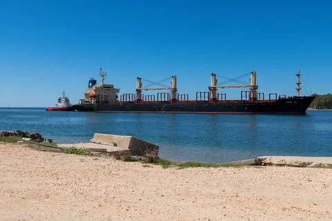 Tugboat escorting cargo ship along rocky coast Fotos Stock