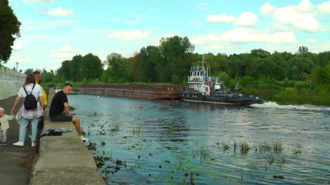 Tugboat moves barge on river with trees and clouds in background 動画素材 340448036