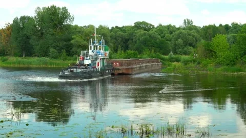 Tugboat moves barge through water in green landscape on a clear day Stock Footage 340448043