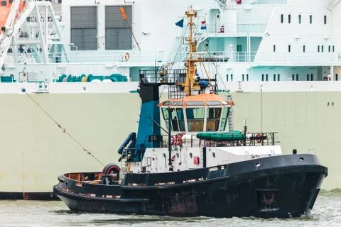 Tugboat pulling a large ship in the dutch rotterdam harbor Stock Photos