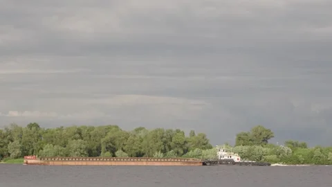A tugboat is pushing a long barge down the wide river Stock Footage 336994872