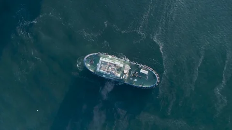Tugboats pull a big ship with a helipad by sea. Look at the scrunch. Aerial Video stock 129614993