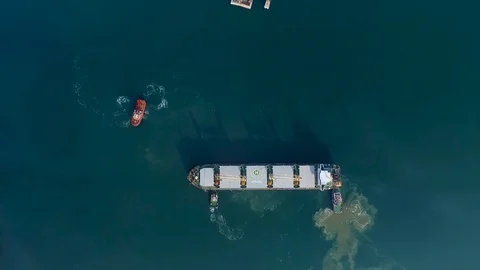 Tugboats push a large cargo ship with containers over a large area of water. Top Video stock 129613929
