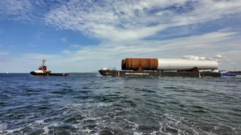 Tugboats towing barge with offshore wind turbine monopiles at sea. Video stock 344972798