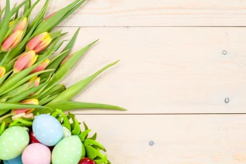 Tulips  with easter eggs in basket over wooden background. Top view. Backdrop Stock Photos