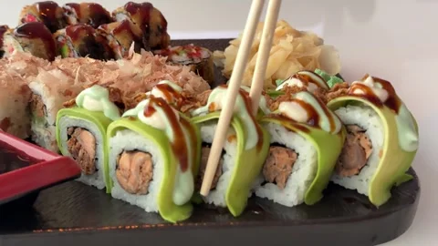 Tuna avocado sushi roll dipped into soy sauce from black sushi platter with Stock Footage 346188377