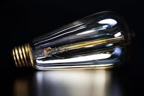 Tungsten light bulb on black reflective surface. Bright idea classic light bulb. Stock Photos