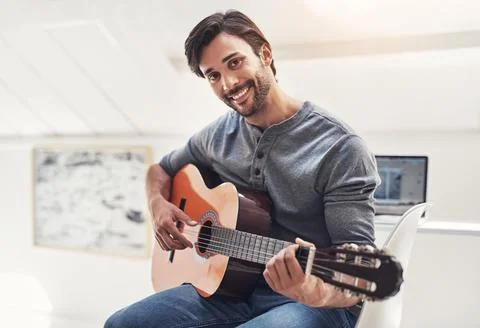 Tuning into his musical talent. a handsome young man practising guitar at home. Stock Photos