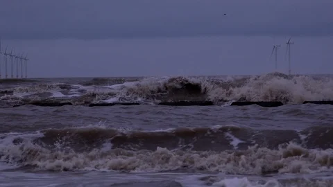 Turbines out at sea with waves breaking on the shore 4K Stock-Footage 101893083