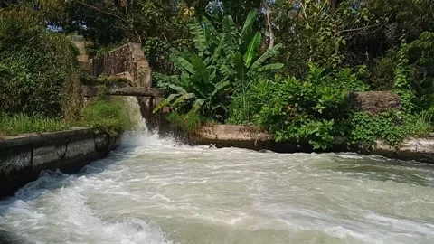 Turbulent canal stream flowing beneath a stone aqueduct near green tropical Stockbeeldmateriaal 345808521