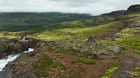Turbulent mountain stream rushing through mossy basalt plateau beneath low Stock Footage 343796512