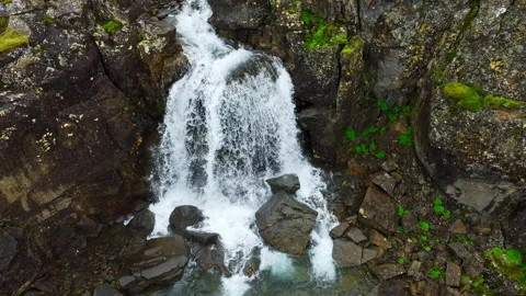 Turbulent mountain stream rushing through mossy basalt plateau beneath low Stock Footage 343796574