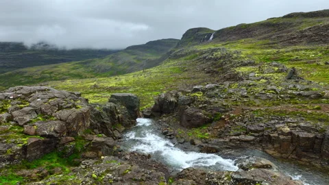 Turbulent mountain stream rushing through mossy basalt plateau beneath low Stock Footage 343796608
