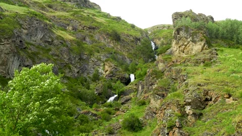 A turbulent stream among rocks: a waterfall framed by wild greenery Stock Footage 342713719
