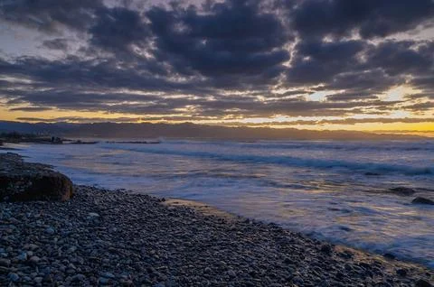 Turbulent waves and dramatic clouds embrace the sunset on a rocky shoreline Foto stock