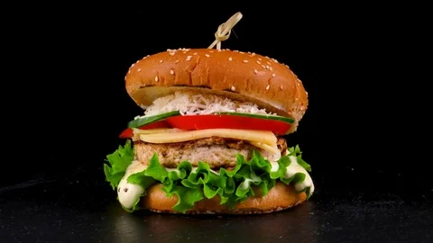 Turkey burger with cheese, fresh vegetables and sauce, on black stone tray Stock Footage 84653156