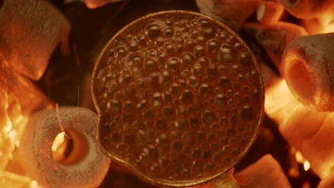 Turkish coffee pot is set on a slow-burning fire. The camera zooms in and out. Stock Footage 128466028