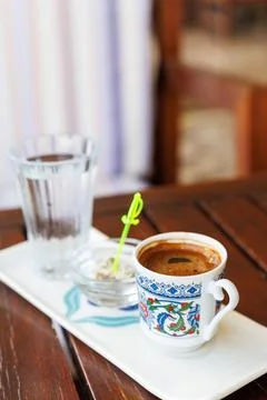 Turkish coffee served in patterned cup with glass of water and small dish with Stock Photos