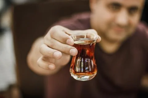 Turkish man holds out black Turkish tea in a traditional glass Stock Photos
