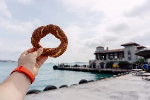 Turkish simit in hand with bay in background. Hot sesame bun with sea in ba.. Stock Photos