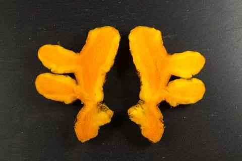 Turmeric root sliced and two halves open on dark slate background Stock Photos