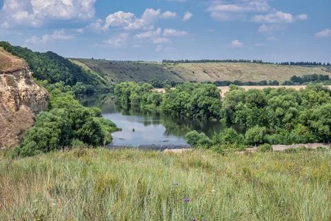 A turn of the river with high steep stone banks, covered with lush green trees. Stock Photos