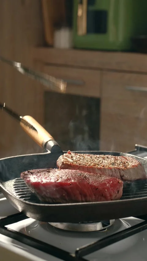 Turn steak over in cast iron griddle pan using kitchen tongs on gas stove at Stock Footage 343794129
