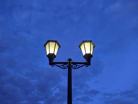 Turned on lamp in the park in the evening against the sky Stock Photos