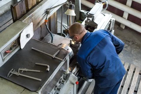 The turner processes the metal part on a mechanical lathe. Stock Photos