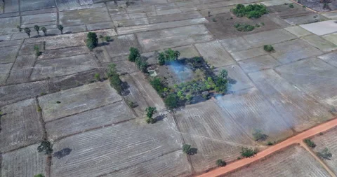 Turning aerial view of a brush fire in parched fields by a red dirt road. Stock Footage 334270421