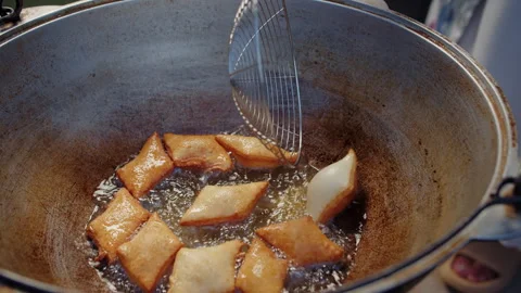 Turning baursak dough pieces while frying in hot oil inside kazan Stock Footage 317752283