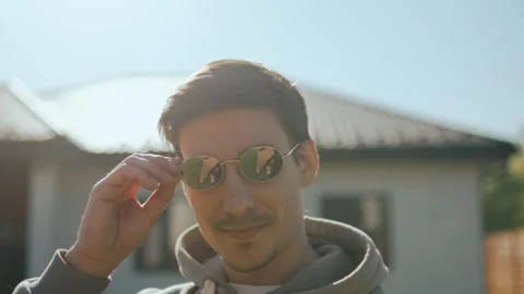 Turning to the camera, a guy in sunglasses smiles and adjusts his glasses Video stock 247655091