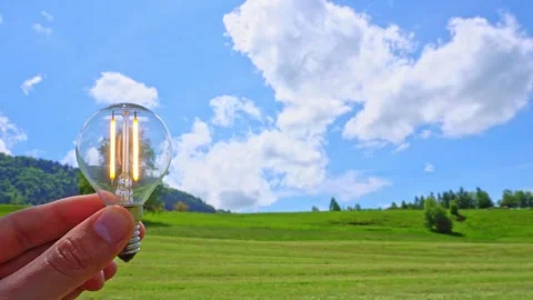 Turning on a light bulb in hands on a beautiful green field with blue sky Stock Footage 276375644