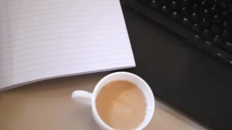 Turning Notebook Page and Holding Coffee Near Laptop Work Setup 動画素材 331351431