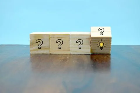 Turning one of many cubes with questionmarks to find an idea symbol on wooden Stock Photos