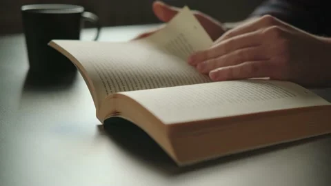 Turning the pages of the book: drinking coffee and reading a book. Video stock 161857508