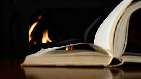 Turning pages of old book next to fireplace, close-up Stock Footage 86999869