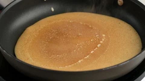 Turning a pancake in a pan. Big round pancake on induction frying pan. Cooking Stock Footage 145490990