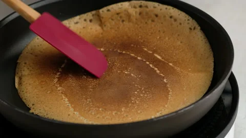 Turning a pancake in a pan. Big round pancake on induction frying pan. Cooking Stock Footage 146907015