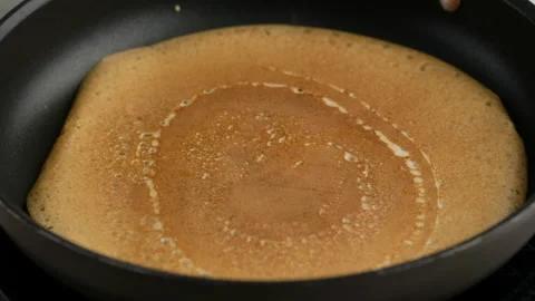 Turning a pancake in a pan. Big round pancake on induction frying pan. Cooking Stock Footage 146907838