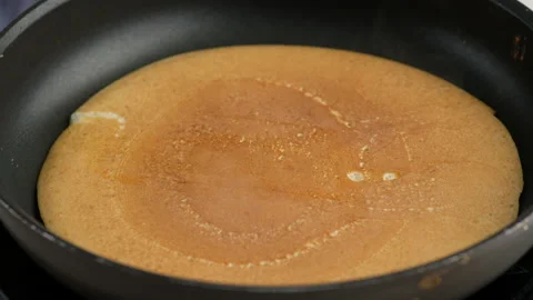 Turning a pancake in a pan. Big round pancake on induction frying pan. Cooking Video stock 148565899