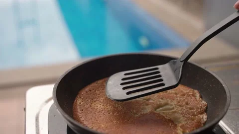 Turning a pancake in a pan. Big round pancake on induction frying pan. Cooking Stock Footage 232367181