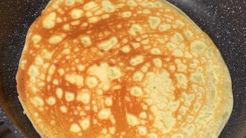 Turning a pancake in a pan. Big round pancake on induction frying pan. Stock Footage 251720616
