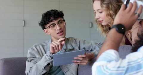 Turning tablet toward friend, Diverse friends on sofa viewing screen as man Stock Footage 340069269