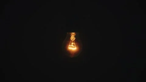 Turns on warm color light incandescent bulb flickers pulsates against a black Stock Footage 346517022