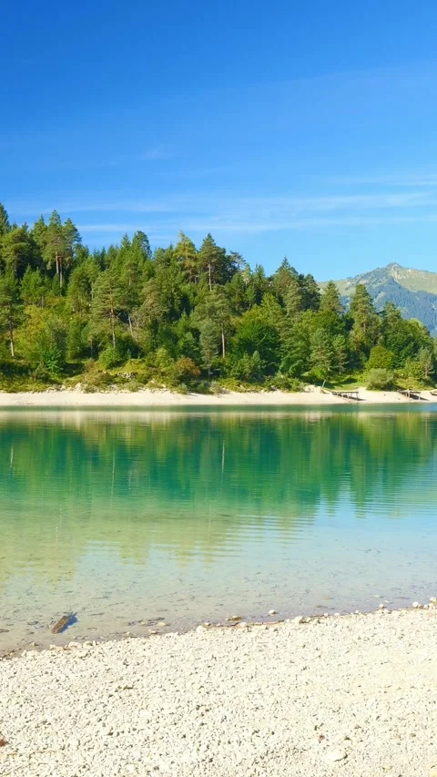 Turquoise alpine lake surrounded by forested mountains and calm shoreline in Stock Footage 308299759