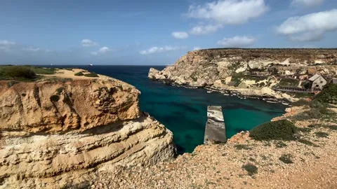 Turquoise cove anchor bay limestone cliffs wooden jetty coastal buildings malta Видео 343680201
