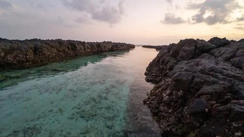 Turquoise lagoon between dark rocks at sunset Stock Photos
