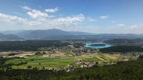 Turquoise Lake Faak glistens amid colorful patchwork farmland and small 動画素材 337908071